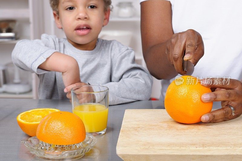 蹒跚学步的小孩/小男孩在看看护人/妈妈在做新鲜橙汁